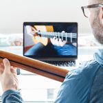 Back view of man taking guitar lessons at home.