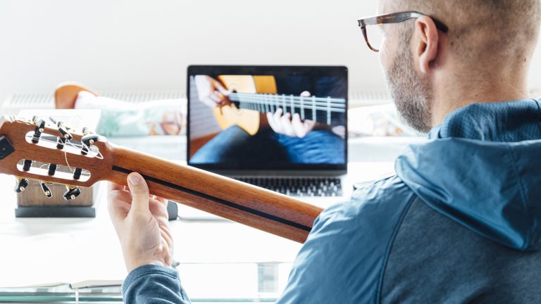 Back view of man taking guitar lessons at home.